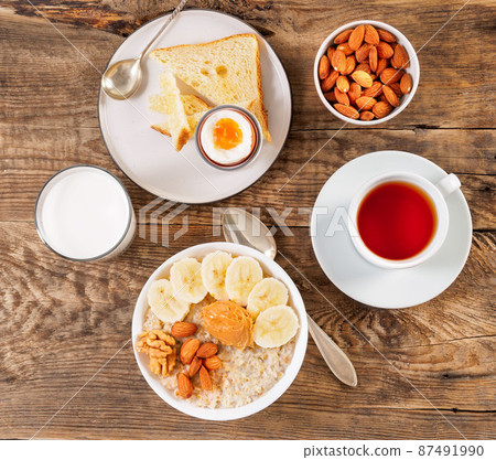 Breakfast in the morning, on a wooden table, top view. A glass of milk, tea, oatmeal with fruits and nuts, soft-boiled egg. Breakfast in the morning, on a wooden table, top view. A glass of milk, tea, oatmeal with fruits and nuts, soft-boiled egg. 87491990