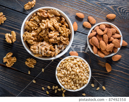 assorted nuts in white bowl on wooden dark background, mix of walnuts, almonds and cedar, top view 87492358