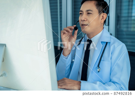 Doctor wearing headset talking actively on video call in a clinic or hospital . Doctor wearing headset talking actively on video call in a clinic or hospital . 87492816