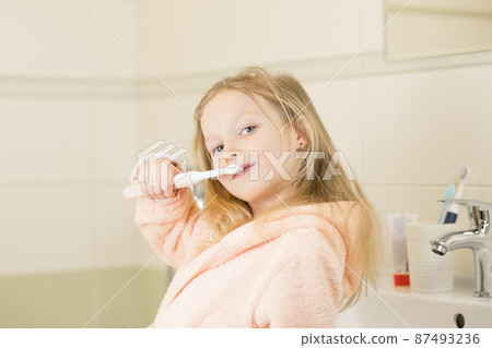 Happy smiling little girl brush teeth using ultrasonic electric toothbrush in bathroom at home. Oral hygiene, dental and gum health, healthy teeth. Daily life and routine. 87493236