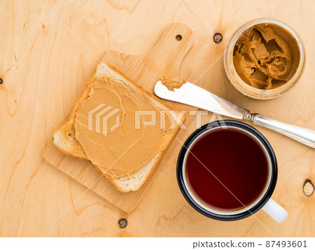 toast with peanut butter, knife for spreading on a sandwich, a mug of tea on a beige wood background toast with peanut butter, knife for spreading on a sandwich, a mug of tea on a beige wood background 87493601
