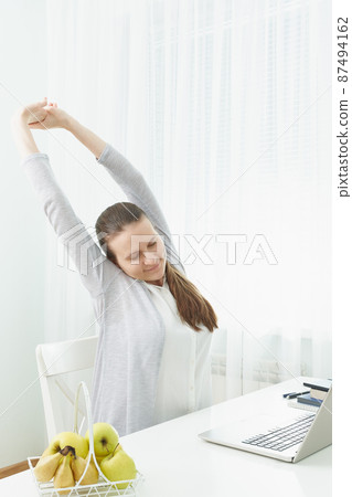 Woman stretches her arms, kneads her back from fatigue. Long sitting at computer, muscle cramps. Woman stretches her arms, kneads her back from fatigue. Long sitting at computer, muscle cramps. 87494162