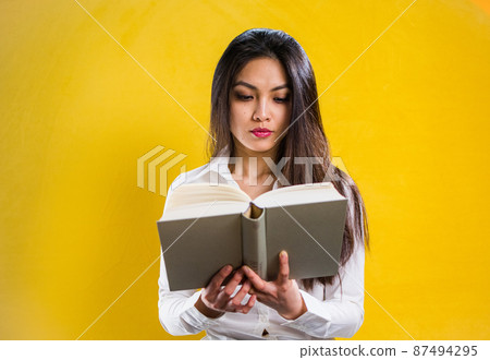Young woman reading a book - studio shot against yellow background Young woman reading a book - studio shot against yellow background 87494295