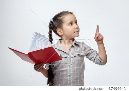 little black-haired girl holds a red book in her hands and points to the free space with her index finger little black-haired girl holds a red book in her hands and points to the free space with her index finger 87494641