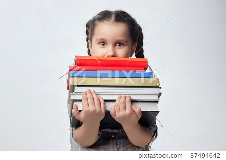 little girl holds a large stack of books in front of her. photo shoot in the studio on a white background 87494642