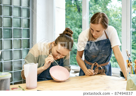 Young skillful pottery master teaching apprentice sculpting and painting mud bowl in art studio Young skillful pottery master teaching apprentice sculpting and painting mud bowl in art studio 87494837
