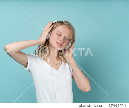 Portrait of young woman listening music via headphones on color neutral tone Aqua Menthe 87494924