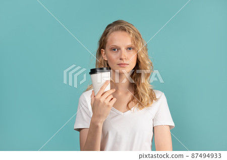 Portrait of young student girl with cup of coffee on color neutral tone blue wall 87494933