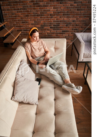 Attractive woman with prosthesis arm in casual wear sitting at the sofa Attractive woman with prosthesis arm in casual wear sitting at the sofa 87495224
