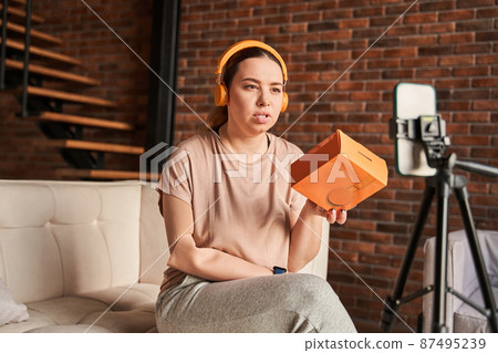 Female blogger with prosthesis limb wearing headphones holding box from it and telling Female blogger with prosthesis limb wearing headphones holding box from it and telling 87495239