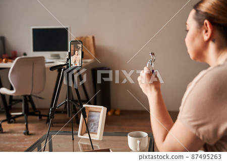 Caucasian blogger talking to camera and showing lushes curler while recording blog about makeup Caucasian blogger talking to camera and showing lushes curler while recording blog about makeup 87495263