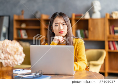 Unhappy frowning asian woman forgetting smth working on laptop 87495937