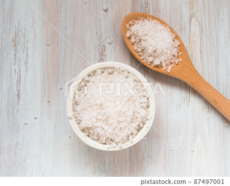 White bowl with large sea salt and wooden spoon on white wooden table. 87497001