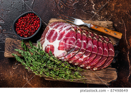 Sliced cured coppa ham on wooden board with thyme. Dark background. Top view 87498649