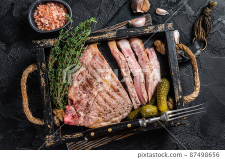 Roasted on grill Pork steaks from neck meat in wooden tray with herbs. Black background. Top view Roasted on grill Pork steaks from neck meat in wooden tray with herbs. Black background. Top view 87498656
