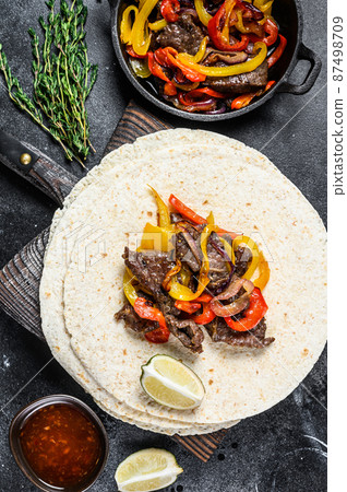 Mexican Fajitas with colored pepper and onions, served with tortillas and salsa. Black background. Top view Mexican Fajitas with colored pepper and onions, served with tortillas and salsa. Black background. Top view 87498709