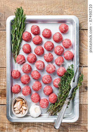 Recipe for cooking meatballs from ground beef with thyme and rosemary in kitchen tray. Wooden background. Top view Recipe for cooking meatballs from ground beef with thyme and rosemary in kitchen tray. Wooden background. Top view 87498710