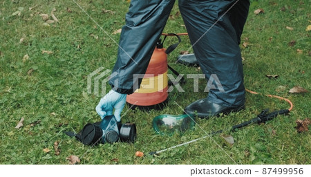 Lawn treatment with insecticides and toxins from ixodic mites and other blood sucking parasites. A man in a protective suit sprays poison on the grass 87499956