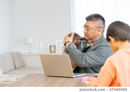 一個在家工作的男人一邊抱著嬰兒一邊工作 一個在家工作的男人一邊抱著嬰兒一邊工作 87499989