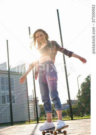 Woman riding a skateboard on street. Skater girl on a longboard. Cool female skateboarder at sunset. Carefree female skater 20s enjoying freedom youth lifestyle Hobby 87500982