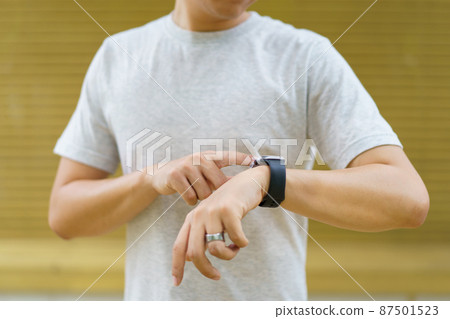 Active Asian young sportsman using a smartwatch or smart fitness band to track his outdoor workout and activities, man reviewing an exercise and health information after finished outdoor workout. 87501523