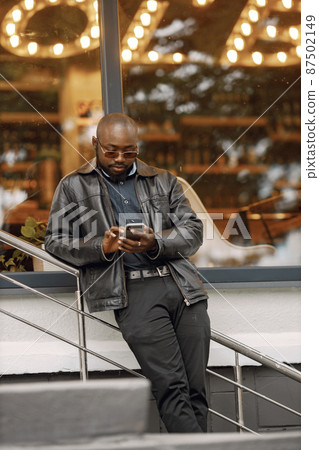 Black man standing on a street and using a phone 87502149