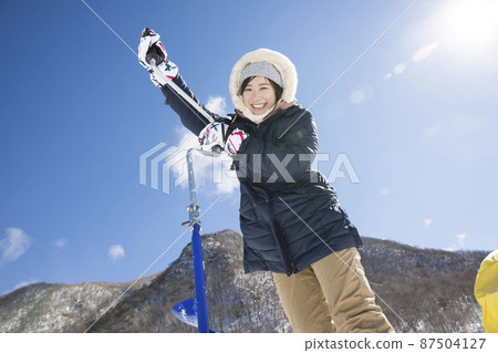 Image of smelt fishing for a woman who drills a hole in the ice of a lake 87504127