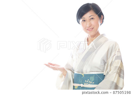 一位中年婦女面帶微笑地看著鏡頭，穿著夏季和服舉起一隻手 87505198