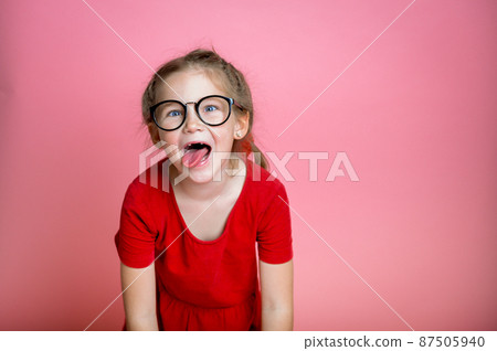 Portrait of silly little child boy in red shirt in glasses mowing eyes, smiling and showing tongue in camera, making funny faces. School kid face with crazy face. Happy nerd child. Back to school 87505940