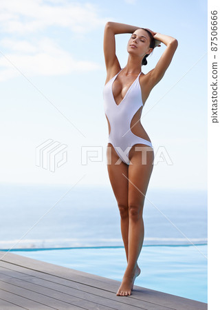 Blissfully sun-kissed. A beautiful young woman posing in a swimming costume next to a pool. 87506666