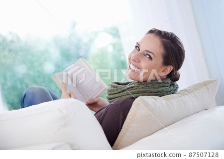 This novel is so engrossing. A relaxed young woman reading an engrossing novel on her couch. 87507128