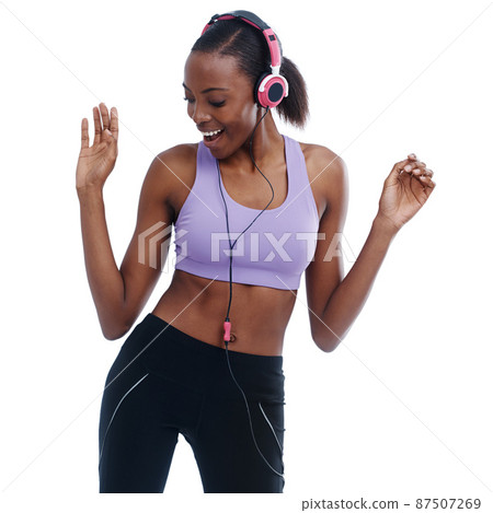 Moving to the beat. A woman in sportswear happily listening to music with her headphones. Moving to the beat. A woman in sportswear happily listening to music with her headphones. 87507269