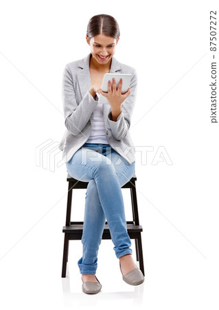 Theres always something new on the net. Studio shot of a beautiful young woman sitting on a stool and using a digital tablet against a white background. 87507272