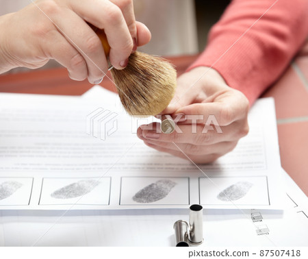 Detailed examination to catch the criminal. Cropped shot of a forensic scientist dusting a bullet above a print out of fingerprints. 87507418