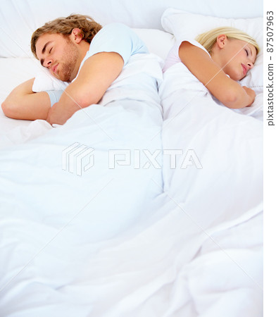 At odds with one another. A young couple sleeping back to back in bed. At odds with one another. A young couple sleeping back to back in bed. 87507963