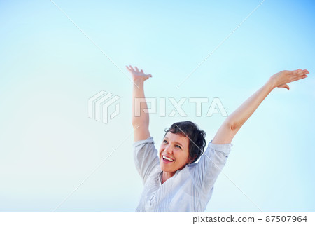 Pure joy. Happy mature woman enjoying freedom against blue sky with arms raised. 87507964