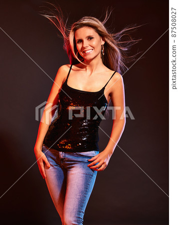 Adding some sparkle to a casual look. A woman posing in a studio wearing jeans and a sparkly black top. 87508027