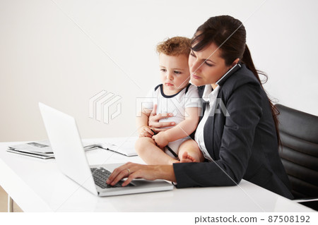 Being a working mom is a balancing act. Working mom talking on the phone while holding a baby and typing on her laptop. 87508192