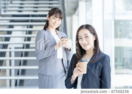 Portrait of two business women standing with a cup in front of the stairs in the business office 87508256