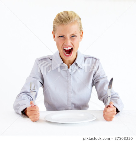 Feed me now. Furious young woman sitting in front of an empty plate while holding her knife and fork. Feed me now. Furious young woman sitting in front of an empty plate while holding her knife and fork. 87508330