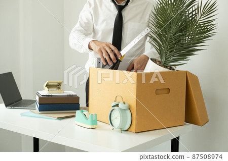 A male office worker is unhappy with being fired from a company packing things into cardboard boxes. The young man was stressed and disappointed by being fired. concept of layoffs and unemployment A male office worker is unhappy with being fired from a company packing things into cardboard boxes. The young man was stressed and disappointed by being fired. concept of layoffs and unemployment 87508974