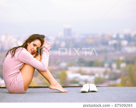 Playtime in the city. Young woman on a rooftop with her shoes off and the city in the background. 87509265