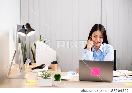 Asian woman working on a laptop with a cheerful and happy smile while working at the office 87509852