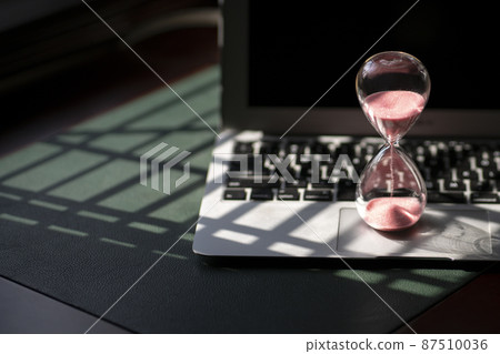 Hourglass sand timer on top of laptop. Hourglass sand timer on top of laptop. 87510036