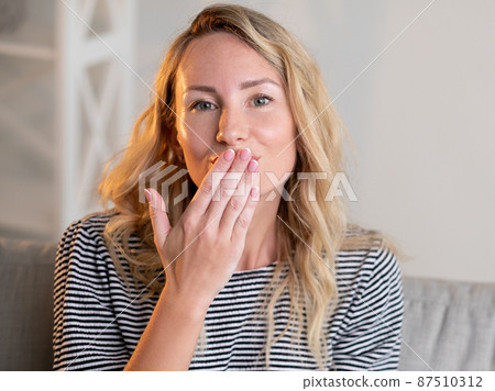 Blowing kiss. Pretty woman. Beloved expression. Smiling beautiful lady casual look sending love message with hand sitting sofa light room interior. Blowing kiss. Pretty woman. Beloved expression. Smiling beautiful lady casual look sending love message with hand sitting sofa light room interior. 87510312