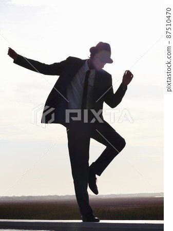 Get up and go. Silhouette image of a young man in a suit dancing against the morning sky. Get up and go. Silhouette image of a young man in a suit dancing against the morning sky. 87510470