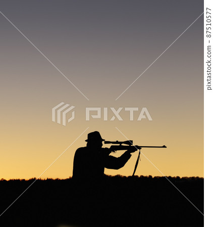 Preparing to shoot. A silhouette of a man in the outdoors holding up his sniper rifle. Preparing to shoot. A silhouette of a man in the outdoors holding up his sniper rifle. 87510577