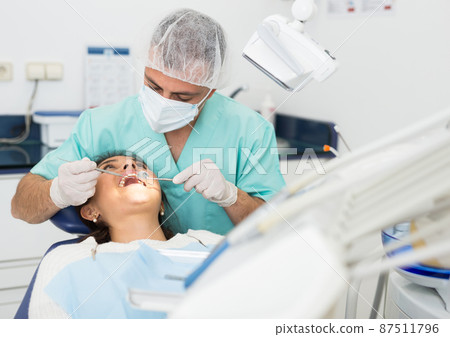 Dentist man examining a latin female patient teeth 87511796