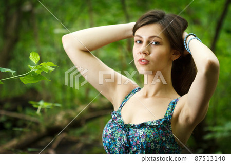 Beautiful young woman wearing elegant white dress walking on a forest path with rays of sunlight beaming through the leaves of the trees 87513140