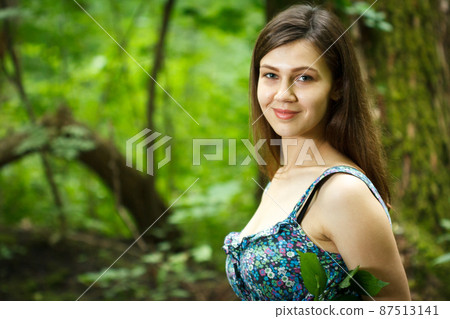 Beautiful young woman wearing elegant white dress walking on a forest path with rays of sunlight beaming through the leaves of the trees 87513141